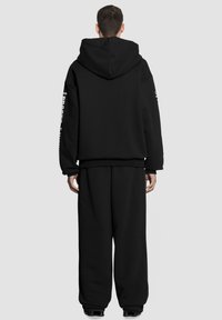 Czarna bluza z kapturem, z długimi rękawami i luźnym krojem. Zawiera detal tekstowy wzdłuż rękawa. W połączeniu z luźnymi czarnymi spodniami.