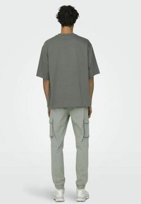 T-shirt gris à manches courtes avec une coupe décontractée, associé à un pantalon cargo gris clair avec poches latérales et poignets élastiques, porté avec des baskets blanches.