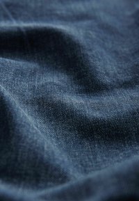 Țesătură de denim de culoare albastru închis, prezentând o suprafață moale, texturată și variații subtile în țesătură și strălucire.