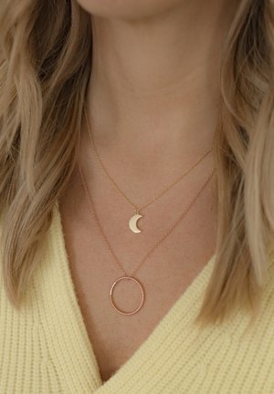 Collares en capas que presentan un colgante en forma de luna creciente dorada y un colgante circular en oro rosa sobre cadenas delicadas. Detalles texturizados en el cierre y la cadena.
