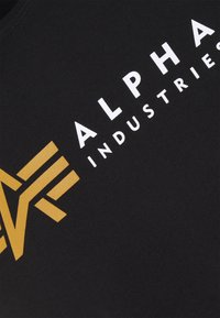 Black cotton T-shirt featuring a large yellow graphic logo and white text "ALPHA INDUSTRIES" on the front, with smooth, soft texture.