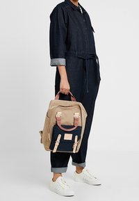 Beżowy i granatowy plecak z wyściełanymi paskami, klamrami i przednią kieszenią; wykonany z trwałego materiału; w kształcie prostokąta.