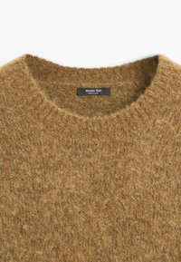 Maglione di lana marrone con una texture morbida e pelosa. Collo a giro e un'etichetta all'interno del collo. Design semplice e uniforme senza decorazioni.