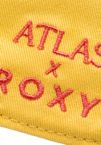 Yellow fabric features red embroidered text. Letters include "ATLAS" and "x ROXY," with various styles and sizes of stitching.