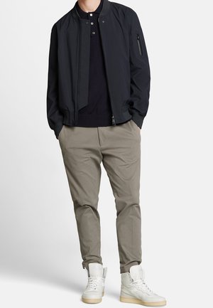 Blouson aviateur bleu marine avec col côtelé, chinos gris clair et baskets montantes blanches. La veste est dotée d'une fermeture éclair et d'une poche latérale.