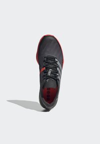 Czarne buty sportowe z szarymi akcentami i czerwoną podeszwą. Posiadają teksturowaną cholewkę, okrągłe sznurowadła oraz wyraźne logo w pobliżu pięty.