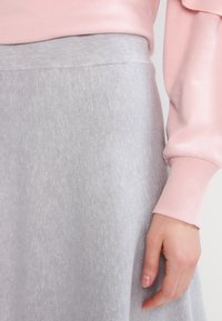 Šedá pletená sukně s ribbovým texturem, kombinovaná s růžovým topem s dlouhým rukávem. Pas je hladký a dobře padnoucí, což vytváří strukturovaný vzhled.