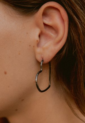 Schwarze Metall-Ohrringe mit einer wellenförmigen, herzähnlichen Gestalt. Die Oberfläche ist glatt und glänzend und zeigt ein modernes Design.