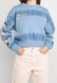 Modrý tie-dye svetr se nápisem "HELLO KITTY"; na rukávech jsou kreslené designy kočičky; žebrované manžety a lem.