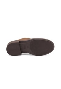 Suela de zapato de ante marrón con una suela exterior de goma texturizada en marrón. Presenta una forma redonda y un logo sutil embosado cerca del talón.