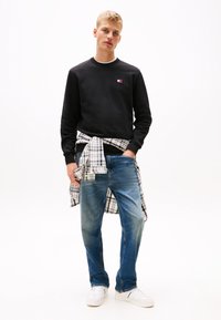 Black sweatshirt with a small logo, blue jeans, and white sneakers. A plaid shirt is tied at the waist. Simple, casual design.