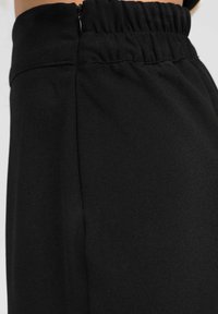 Pantalons de jogging noirs avec une texture de tissu lisse et une taille élastique. Présente une fermeture éclair sur le côté pour un enfilage facile.