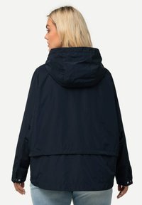 Marinblå lättviktsjacka med huva, med en avslappnad passform, tryckknappar och en något längre bakre fåll. Slät textur och minimal design.