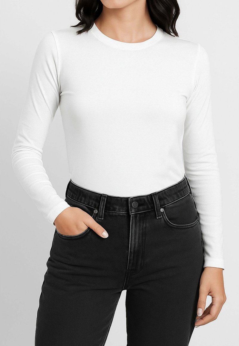 Top bianco aderente a maniche lunghe in tessuto liscio, abbinato a jeans neri a vita alta con tasche standard e chiusura con bottone.