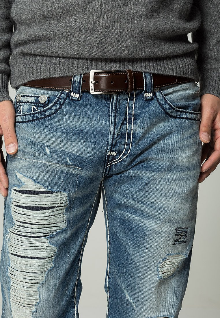 Falmede blå jeans med slidte lapper, frynset kant og kontrasterende søm. Akkompagnert av et mørkebrunt lærbelte.