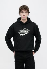 Μαύρο φούτερ με κουκούλα από βαμβάκι, με μεγάλο λευκό λογότυπο στο κέντρο. Διαθέτει μπροστινή τσέπη και κουκούλα με ρυθμιζόμενο κορδόνι.