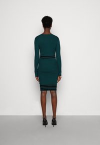 Abito attillato con maniche lunghe in maglia a coste di color teal, con strisce orizzontali nere in vita e all'orlo. Abbinati a scarpe col tacco nere.