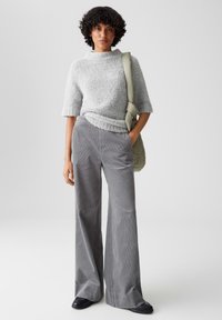 Pullover grigio a trama con maniche corte abbinato a pantaloni a gamba larga in corduroy grigi a vita alta e una morbida borsa a spalla grigia.