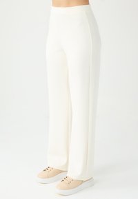 Pantalons larges blancs à taille haute avec des lignes épurées, associés à des baskets beige clair. Tissu lisse et texturé.