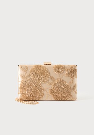 Suorakulmainen beige clutch-laukku, jossa on kullanvärinen kukka kirjailu ja kullanvärinen ketjuhihna yksivärisellä taustalla.
