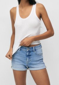 Valkoinen puuvillainen tankkitoppi ja vaaleansiniset farkkushortsit käännetyillä lahkeilla. Shortseissa on napitus ja etutaskut.