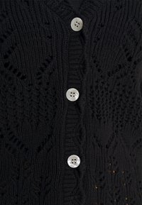 Svart stickad cardigan med ett strukturerat mönster och fem stora, runda knappar med fyra hål framtill.