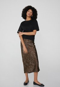 Haut noir à manches courtes associé à une jupe midi en satin imprimé léopard, avec une texture lisse et une silhouette fluide. Chaussures plates noires.