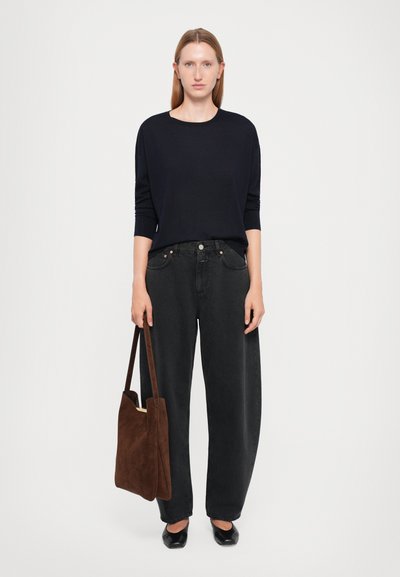Haut à manches longues bleu marine, jeans noirs taille haute à jambes larges, sac fourre-tout en daim marron et chaussures plates noires. Design simple et minimal.
