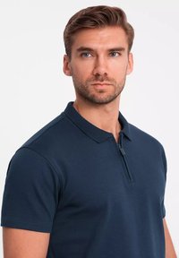 Granatowa koszulka polo z zamkiem błyskawicznym, krótkimi rękawami i kołnierzykiem. Wykonana z teksturowanej, oddychającej tkaniny.