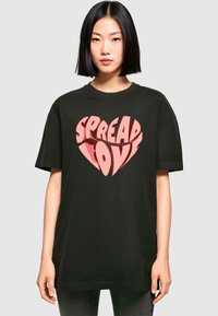 Camiseta de algodón negra con un gran gráfico rosa que dice "SPREAD LOVE" en forma de corazón, con un corte relajado y mangas cortas.