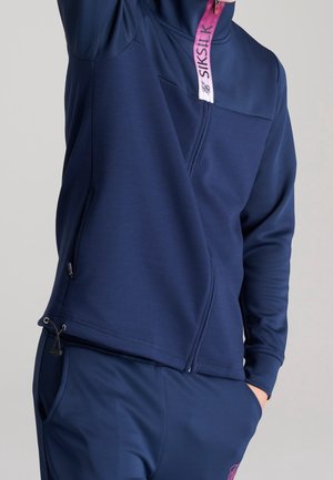 Mørkeblå sweatshirt med lynlås og høj krave, lyserød lynlåstrækker med mærke, sidelommer og elastisk snøre ved kanten.