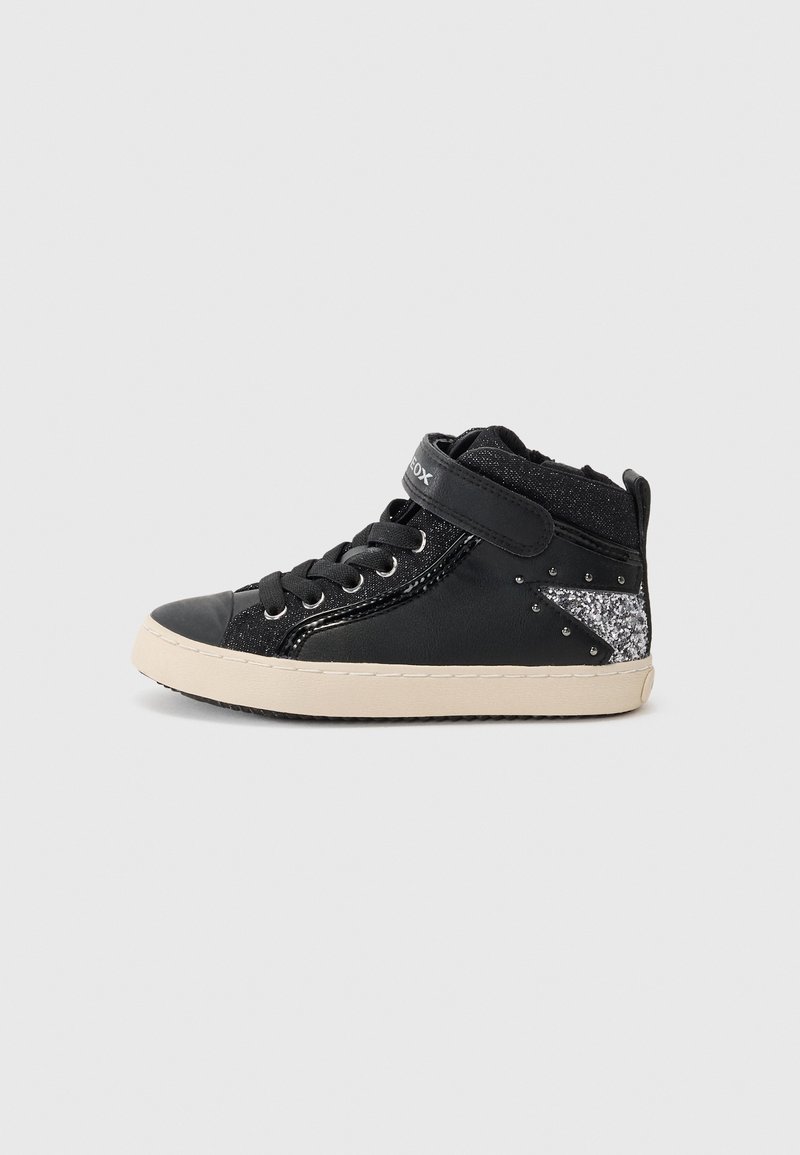 Baskets montantes noires avec semelle blanche, détail étoile argentée pailletée, bande auto-agrippante et lacets noirs, sur fond gris clair uni.