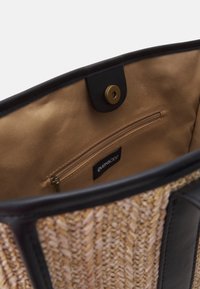 Tkaná slaměná kabelka s černými akcenty, vybavená béžovým saténovým interiérem, zipovou kapsou a magnetickým uzávěrem.