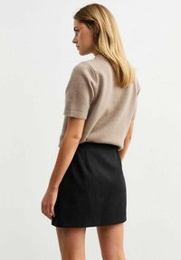 Suéter de punto de color beige claro, de manga corta y cuello redondo, combinado con una falda negra de cintura alta, que presenta una textura suave y un diseño minimalista.