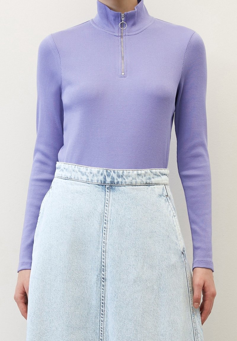 Haut à manches longues côtelé lilas avec un col montant et un détail de fermeture éclair argentée, associé à une jupe en denim bleu clair.