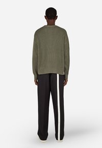 Oliwkowy sweter ze żeberkami zestawiony z czarnymi spodniami typu wide-leg z białym paskiem po bokach, widok z tyłu. Gładka tekstura, luźny krój.