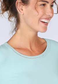 Hellblaues Kurzarmoberteil mit rundem Ausschnitt und Spitzenverzierungen; glatte Textur und figurschmeichelnde Passform.