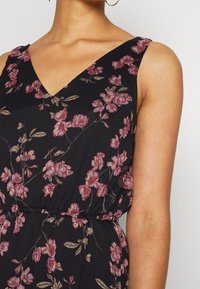 Schwarzes Blumenkleid mit V-Ausschnitt und dünnen Trägern. Besetzt mit rosa Blumen und grünen Blättern, mit einer gerafften Taille für eine bequeme Passform.