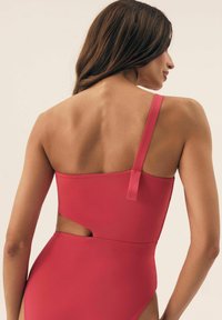 Czerwony kostium kąpielowy na jedno ramię z wycięciem, wykonany z gładkiego materiału, z jedną rączką i minimalistycznym wzorem.