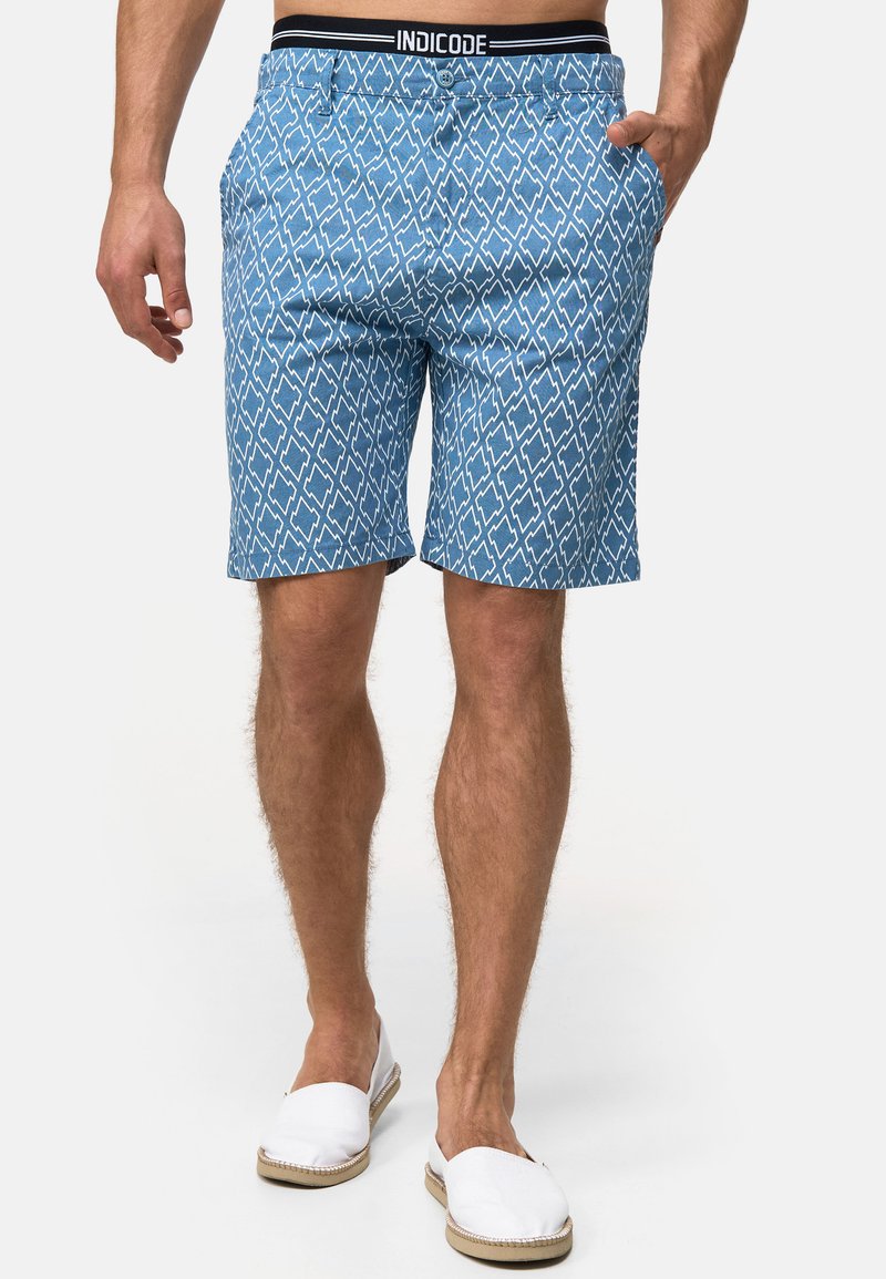 Shorts bleus à motif avec des formes de diamant, fabriqués en tissu léger, dotés de poches et d'une taille élastique avec une marque noire.