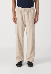 Beżowe spodnie sztruksowe o luźnym kroju, z pionowymi prążkami, elastyczną talią ze sznurkiem oraz kieszeniami po bokach.