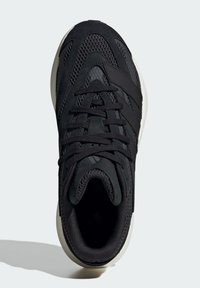 Čierna atletická obuv s vrchnou časťou z sieťoviny, textilnými šnúrkami a kontrastnou bielou podrážkou. Hladké textúry a štruktúrovaný dizajn.