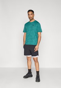 Τιρκουάζ πουκάμισο με κοντά μανίκια και υφή, σε συνδυασμό με μαύρο αθλητικό σορτς με λευκές λεπτομέρειες. Μαύρα παπούτσια ολοκληρώνουν την εμφάνιση.