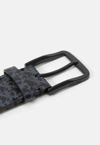 Black patterned belt with a matte finish, featuring a rectangular buckle, and "Calvin Klein" engraved on the side.