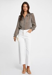 Blusa de estampado marrón y blanco con cuello, combinada con pantalones blancos de cintura alta con detalles de botones y sandalias doradas de tiras.