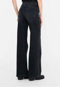 Jeans in denim neri a vita alta con una vestibilità ampia, dotati di due tasche posteriori e una texture liscia. Il tessuto ha una leggera lucentezza.