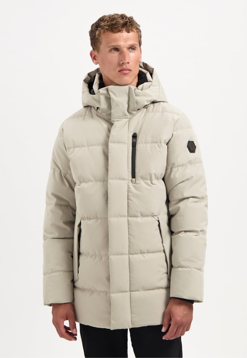 Lichtbeige pufferjack met capuchon, voorzien van een ritszak op de borst, een hexagonale logopatch en gestikte vierkanten voor extra textuur.