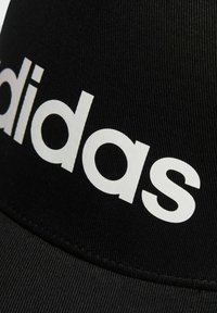 Gorra negra con visera curvada; presenta un prominente logo blanco de "adidas". Está hecha de un tejido texturizado con detalles de costura visibles.