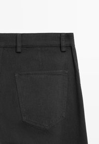 Black denim pants featuring a back pocket with a seam detailing. The waistband includes belt loops and a smooth texture.