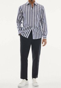 Maglietta a maniche lunghe a righe blu navy e bianca in cotone con scollo a collo, abbinata a pantaloni scuri e sneakers bianche.